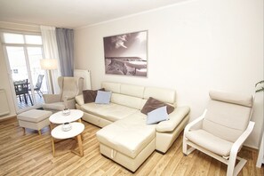 Een woonkamer met een bank, fauteuils, een kleine tafel en een groot raam.