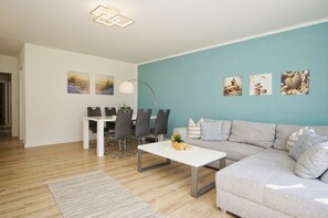 A modern living room with a grey sofa, a white coffee table, and a dining area with a white table and grey chairs.