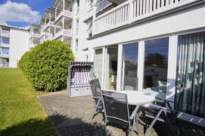 A white building with balconies, a glass door, and a small patio with a table and chairs. - Haus Nordstrand - Holiday apartment with terrace, use of swimming pool and sauna - House (Göhren)