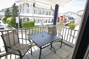 A balcony with a table and two chairs, overlooking a building with a sign reading 'Min.' - Haus Rügen - Vacation apartment with a balcony, access to the pool and sauna - Haus Rügen (Göhren)