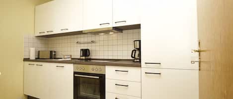 A modern kitchen with white cabinets, a stove, oven, and a coffee maker.