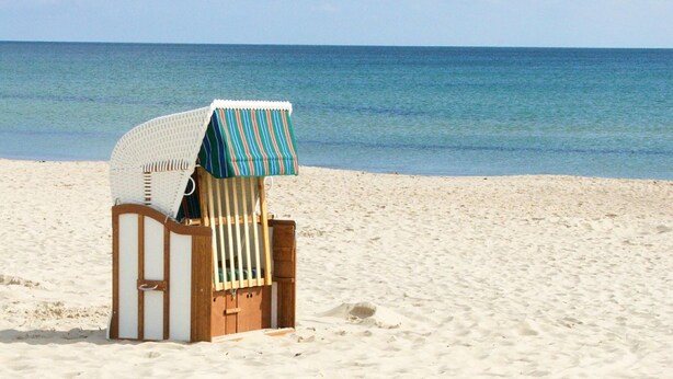 A beach chair with a striped awning on a sandy beach.