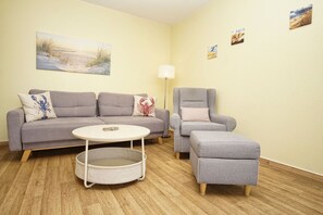 A living room with a grey sofa, a grey armchair, a round white table, and a grey ottoman.