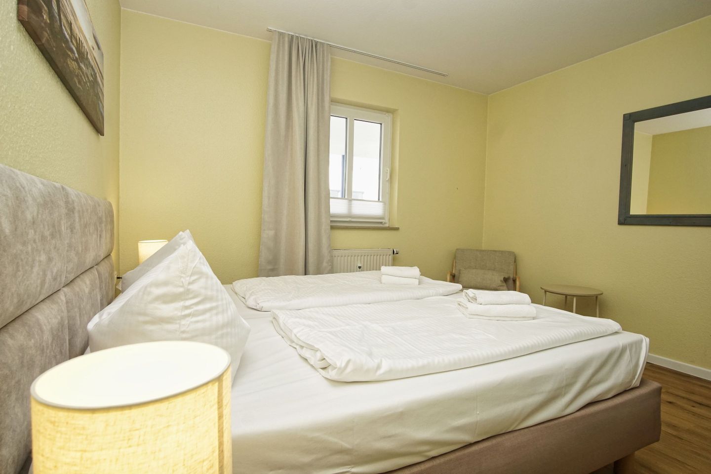 A hotel room with a bed, a chair, a small table, and a window with curtains.