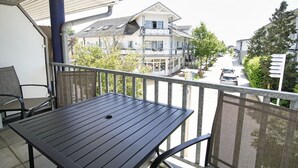 A balcony with a table and chairs, overlooking a street with buildings and trees.