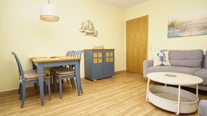 A room with a dining table, chairs, a sofa, a small round table, a cabinet, and a painting on the wall.