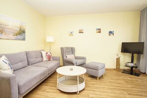 A living room with a sofa, armchair, ottoman, round coffee table, and a flat-screen TV. - Haus Rügen - Vacation apartment with a balcony, access to the pool and sauna - Haus Rügen (Göhren)