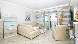 A modern living room with a beige sofa, a glass cabinet, and a painting of sailboats. - FeWo Ostseeperle - with sea view and balcony, use of swimming pool and sauna - FeWo (Göhren)