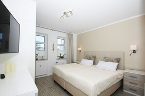 A hotel room with a large bed, bedside tables, a TV, and a window with curtains. - FeWo Ostseeperle - with sea view and balcony, use of swimming pool and sauna - FeWo (Göhren)