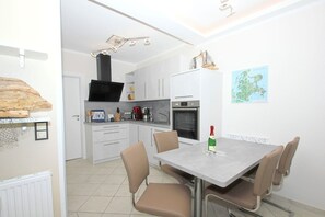 A modern kitchen with white cabinets, a black range hood, and a dining area with a table and chairs.