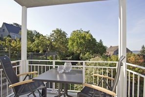 Un espace extérieur aménagé, abrité et doté de tables et de chaises, offrant une vue sur un quartier résidentiel avec ses arbres et ses maisons.