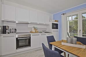 Une cuisine moderne avec des meubles blancs, une cuisinière, un four et un coin repas comprenant une table et des chaises.
