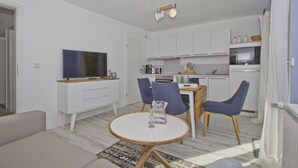 A modern living room with a TV, sofa, and dining area with chairs. - Modern vacation apartment with balcony, sea view - Ferienresidenz Zwei BoddenFeWo 1-2 (Lietzow)