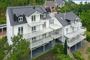Un immeuble résidentiel à plusieurs étages, doté de balcons, d’un toit plat et entouré d’un jardin.