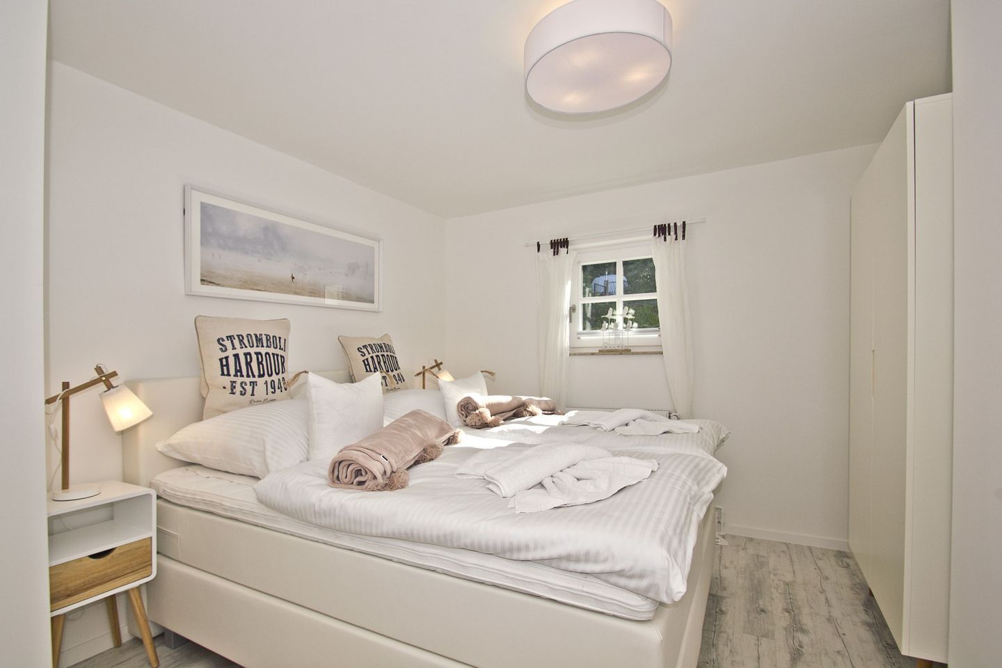 A bedroom with a bed, bedside table, lamp, and a window with curtains.