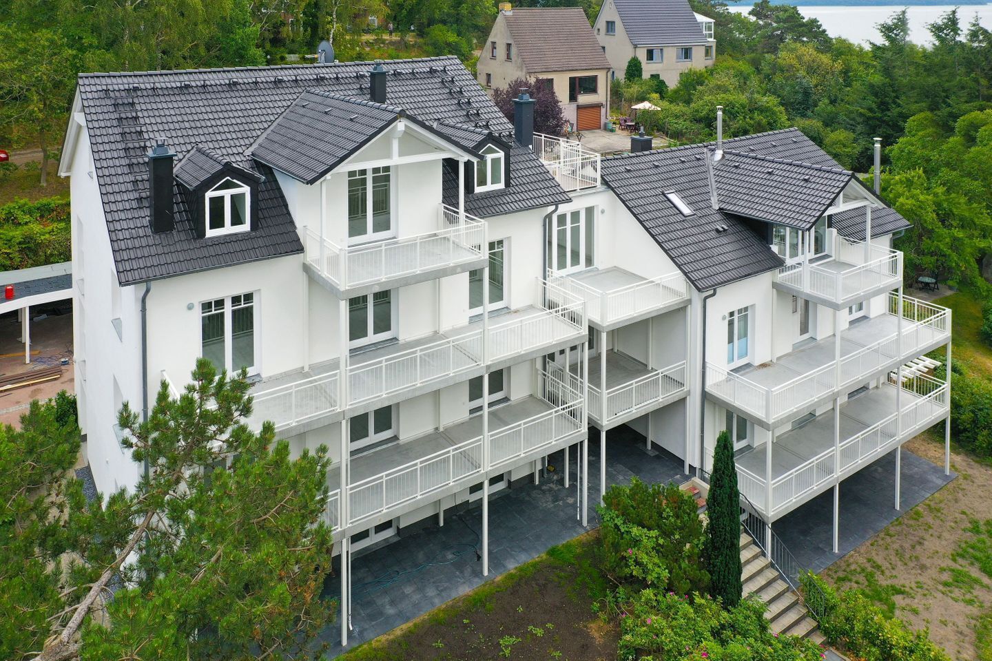 Ein mehrstöckiges Wohngebäude mit Balkonen, einer flachen Dachterrasse und einem umlaufenden Garten.