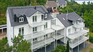 A multi-story residential building with balconies, a flat roof, and a surrounding garden. - Modern vacation apartment with balcony, sea view - Ferienresidenz Zwei BoddenFeWo 1-2 (Lietzow)