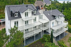 A multi-story residential building with balconies, a flat roof, and a surrounding garden.