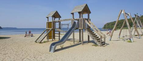 Un parque infantil en la playa con un tobogán y estructuras para escalar.