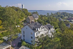 A multi-story building with a prominent tower, surrounded by lush greenery and a lake view.