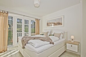 A bedroom with a large bed, a bedside table with a lamp, and a window with curtains.