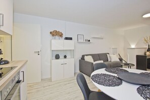A modern, well-lit living area with a grey sofa, a white dining table with black placemats, and a white cabinet with decorative items. - Modern vacation apartment with fireplace, balcony - Ferienresidenz Zwei Bodden FeWo111 - (Lietzow)