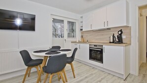 A modern kitchen with white cabinets, a built-in oven, and a dining area with a round table and chairs.