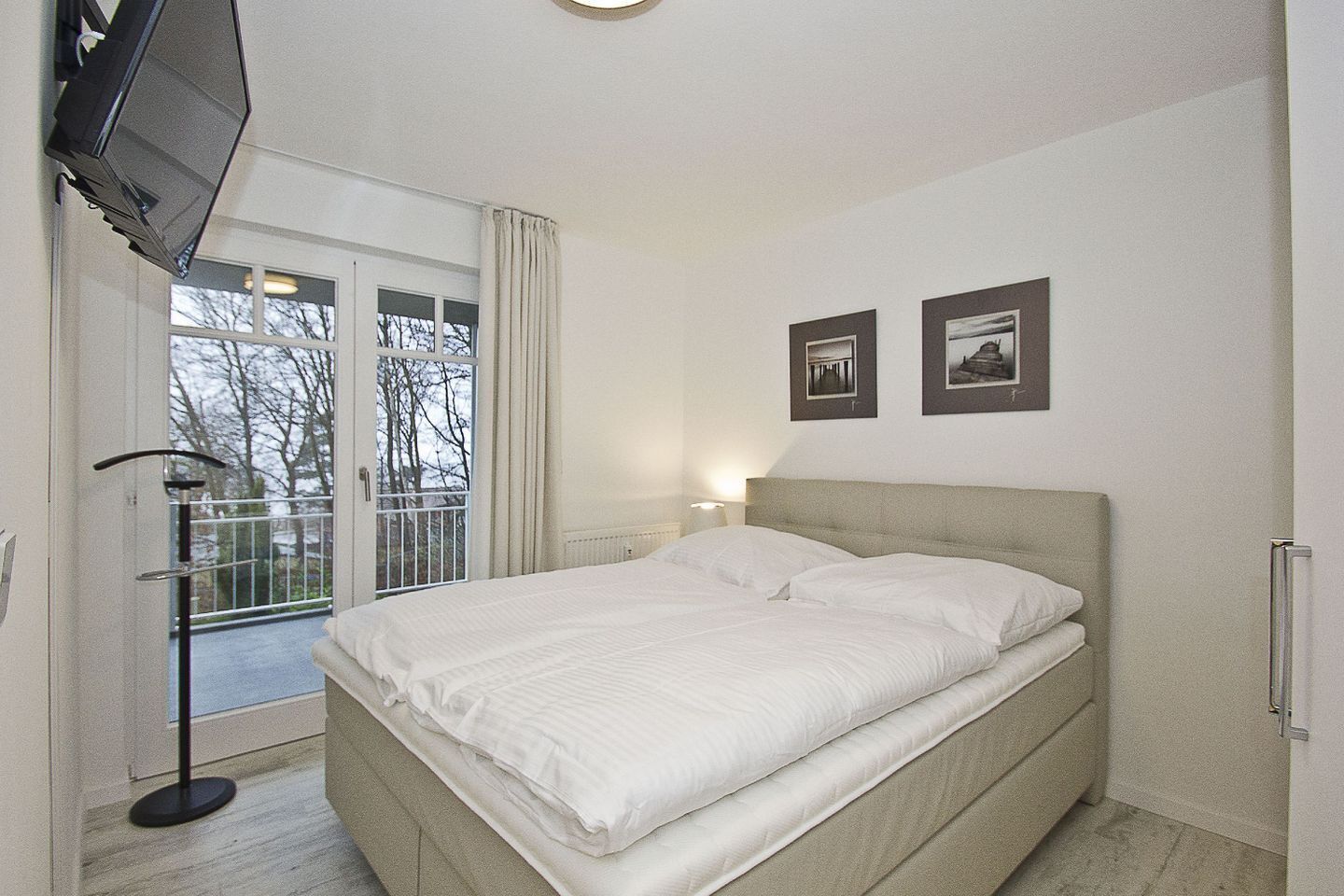 A bedroom with a bed, a TV, a window with curtains, and two framed pictures on the wall.