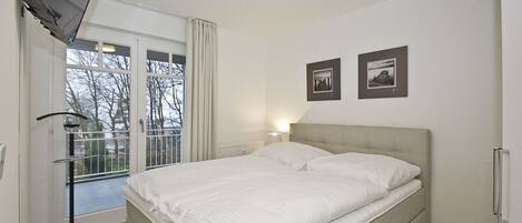 A bedroom with a bed, a TV, a window with curtains, and two framed pictures on the wall.