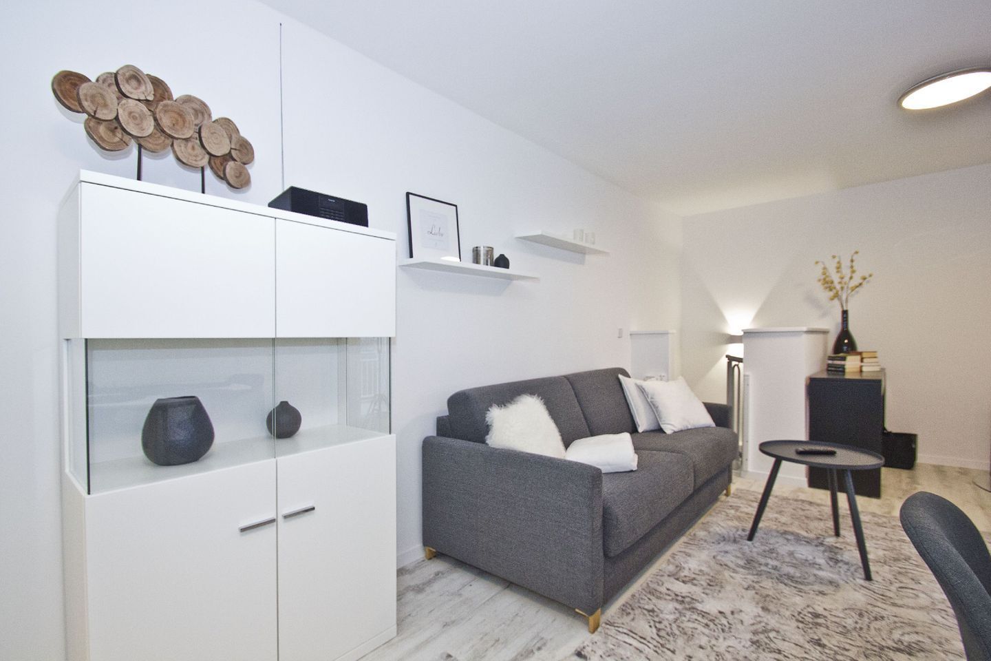 A modern living room with a grey sofa, white shelves, and a decorative wood art piece.