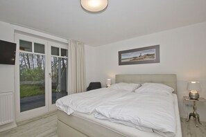 A bedroom with a bed, a chair, a desk, and a window with curtains. - Modern vacation apartment with sauna and terrace - Ferienresidenz Zwei Bodden 112 - (Lietzow)