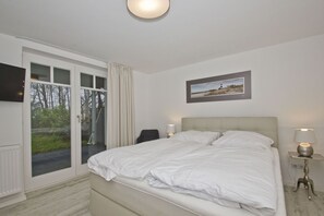 A bedroom with a bed, a chair, a desk, and a window with curtains. - Modern vacation apartment with a sauna and terrace - Ferienresidenz Zwei Bodden 112 - (Lietzow)