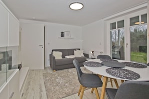 Una sala de estar moderna con un sofá gris, una mesa redonda de comedor con individuales y un aparador de vidrio.
