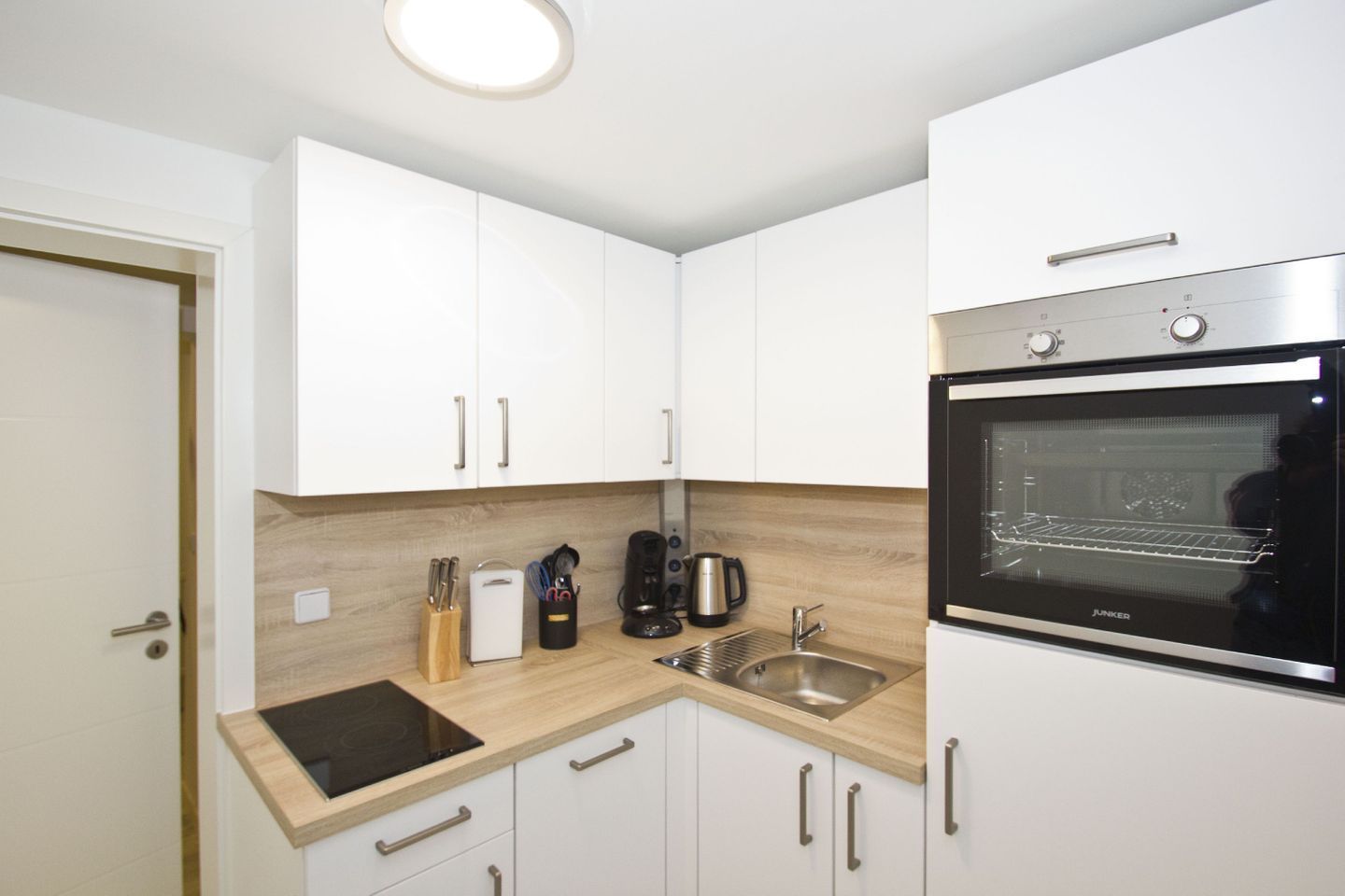 Een compacte keuken met witte kasten, een zwarte oven, een spoelbak en een houten aanrecht.