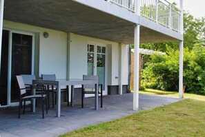 A covered patio with a table and chairs, a sliding glass door, and a balcony. - Modern vacation apartment with sauna and terrace - Ferienresidenz Zwei Bodden 112 - (Lietzow)