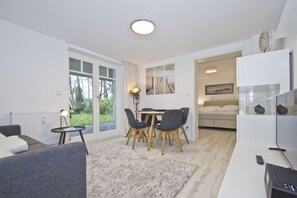 A modern living room with a sofa, a dining table with chairs, a TV, and a fireplace. - Modern vacation apartment with sauna and terrace - Ferienresidenz Zwei Bodden 112 - (Lietzow)