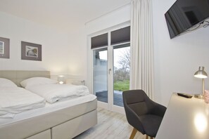 A modern hotel room with a bed, a desk with a lamp, a chair, and a TV on the wall. - Vacation apartment with a terrace, fireplace, and sauna - Ferienresidenz Zwei Bodden FeWo 2-6 - (Lietzow)