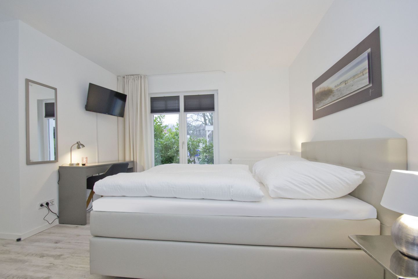 Ett modernt hotellrum med en stor säng, ett skrivbord, en platt-TV och ett fönster med utsikt över grönområden.