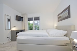 A modern hotel room with a large bed, a desk, a flat-screen TV, and a window with a view of greenery. - Vacation apartment with a terrace, fireplace, and sauna - Ferienresidenz Zwei Bodden FeWo 2-6 - (Lietzow)