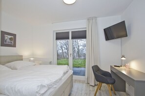 A bedroom with a bed, a desk, a chair, a television, and a view of the outdoors.