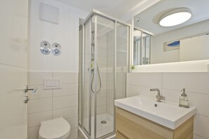 A modern bathroom with a glass-enclosed shower, a white toilet, a sink with a mirror above it, and a light fixture on the ceiling. - Modern 2-room vacation apartment with balcony - Ferienresidenz Zwei Bodden FeWo 1-4 - (Lietzow)
