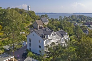 A multi-story building with a flat roof, surrounded by trees and a body of water in the background.