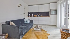 A modern living room with a grey sofa, a coffee table, and a kitchen area with white cabinets and a black countertop.