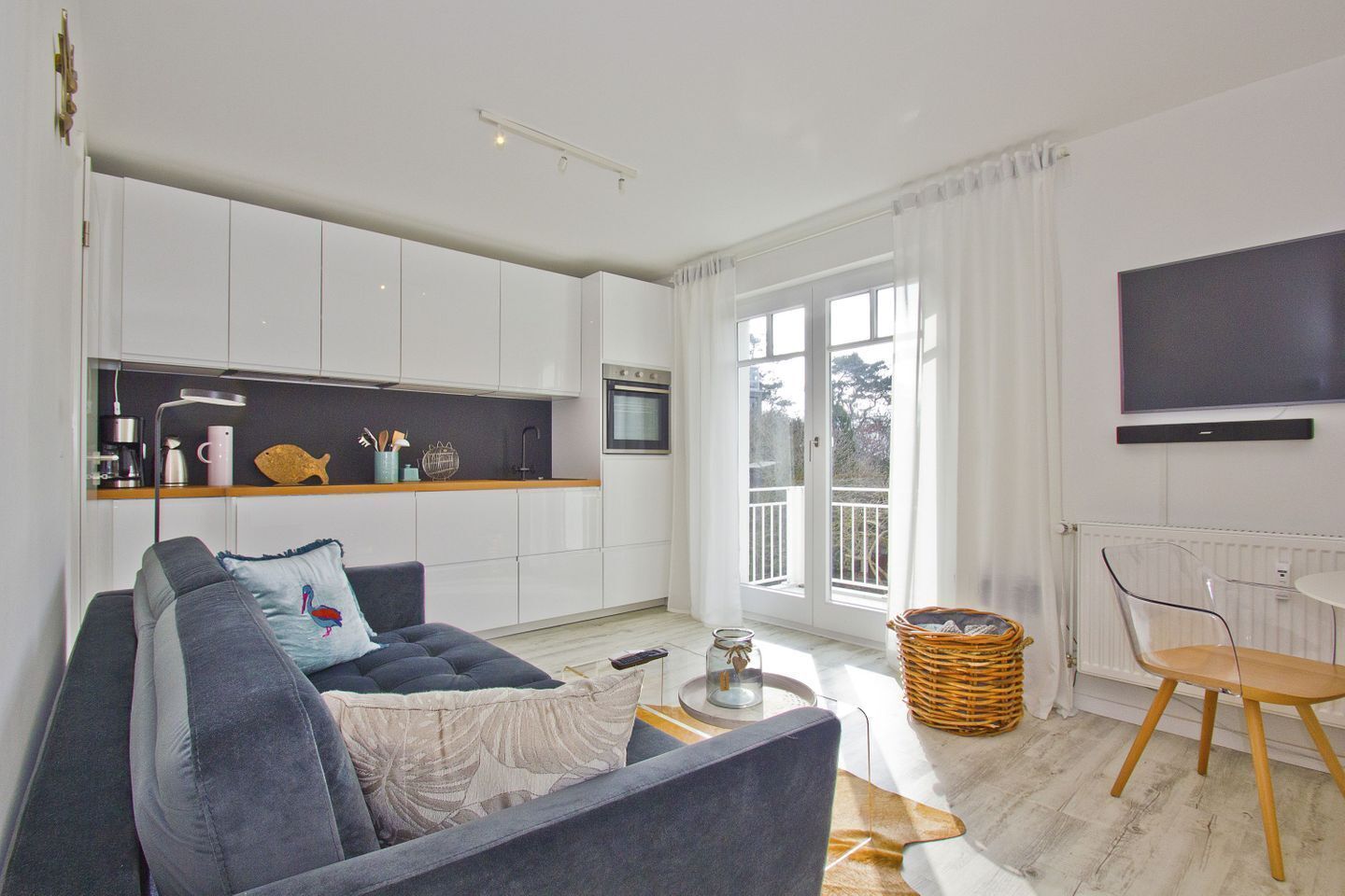 Ein modernes Wohnzimmer mit einer Couch, einem Couchtisch, einem Fernseher und einer Küchenzeile mit Fenster.