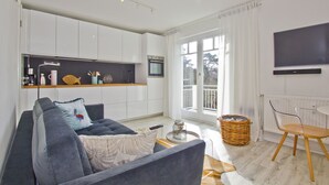 A modern living room with a sofa, a coffee table, a TV, and a kitchen area with a window.