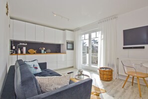 A modern living room with a sofa, a coffee table, a TV, and a kitchen area with a window.