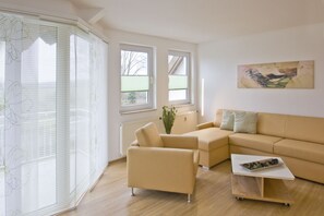 A modern living room with a beige sofa, a coffee table, and a large window with blinds.