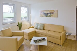 A modern living room with a beige sectional sofa, a small white coffee table, and a painting on the wall. - Close to the beach, with a balcony; access to the pool and sauna - Strandhaus Mönchgut FeWo13 (Middelhagen)