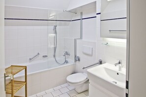 A modern bathroom with a glass-enclosed shower, a white toilet, a sink with a mirror, and a wooden shelf. - Close to the beach, with a balcony; access to the pool and sauna - Strandhaus Mönchgut FeWo13 (Middelhagen)