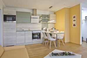 A modern kitchen with a dining area, wooden flooring, and a yellow accent wall. - Close to the beach, with a balcony; access to the pool and sauna - Strandhaus Mönchgut FeWo13 (Middelhagen)